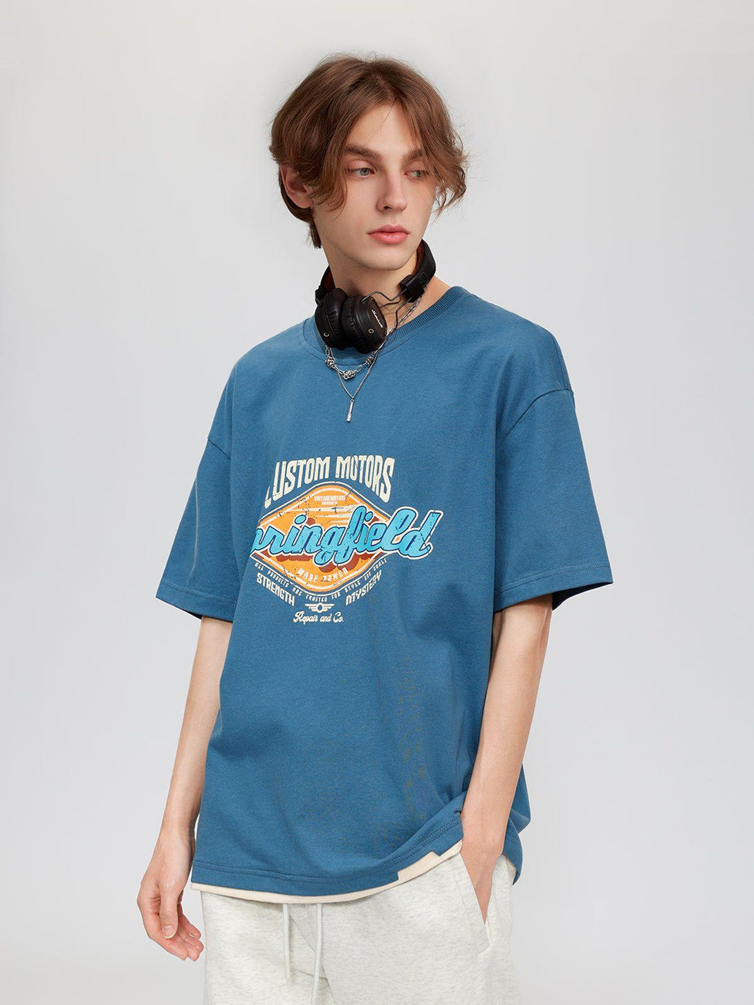 Model wearing a blue graphic tee by TALISHKO, styled with casual headphones.