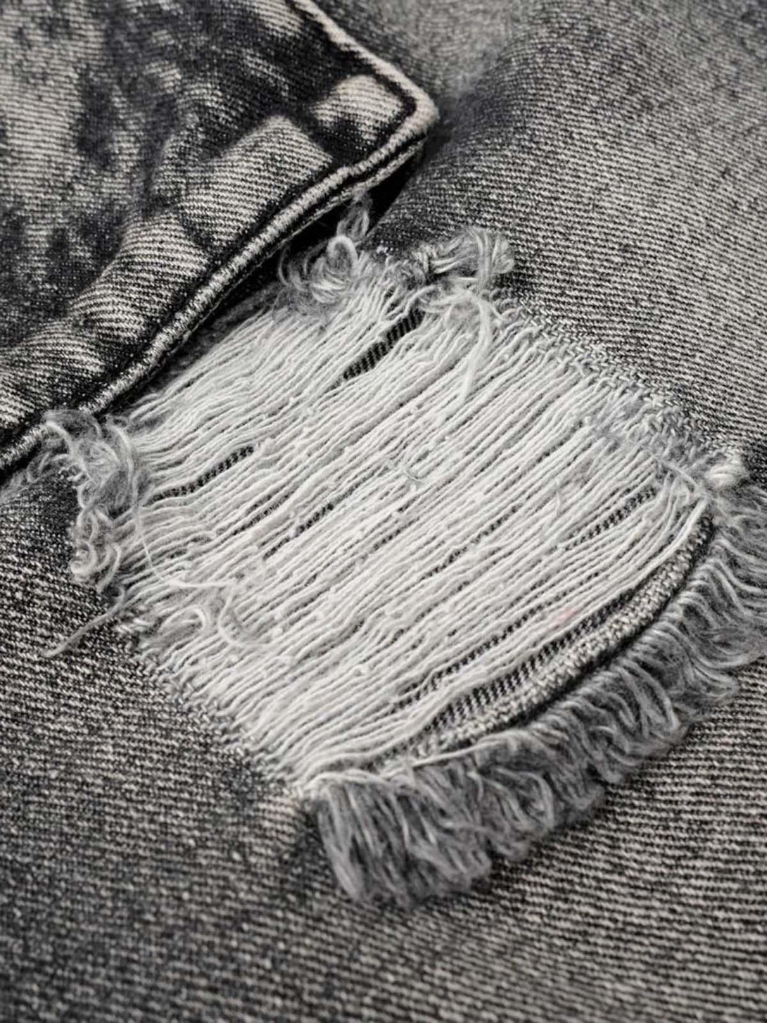 Zoomed-in texture of distressed denim shorts by TALISHKO, showcasing rugged fabric details.