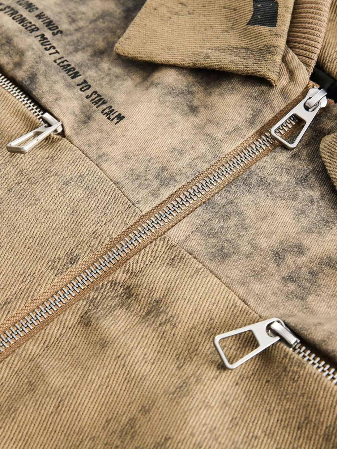 A detailed view of TALISHKO jacket's distressed fabric with double zippers and text accents.