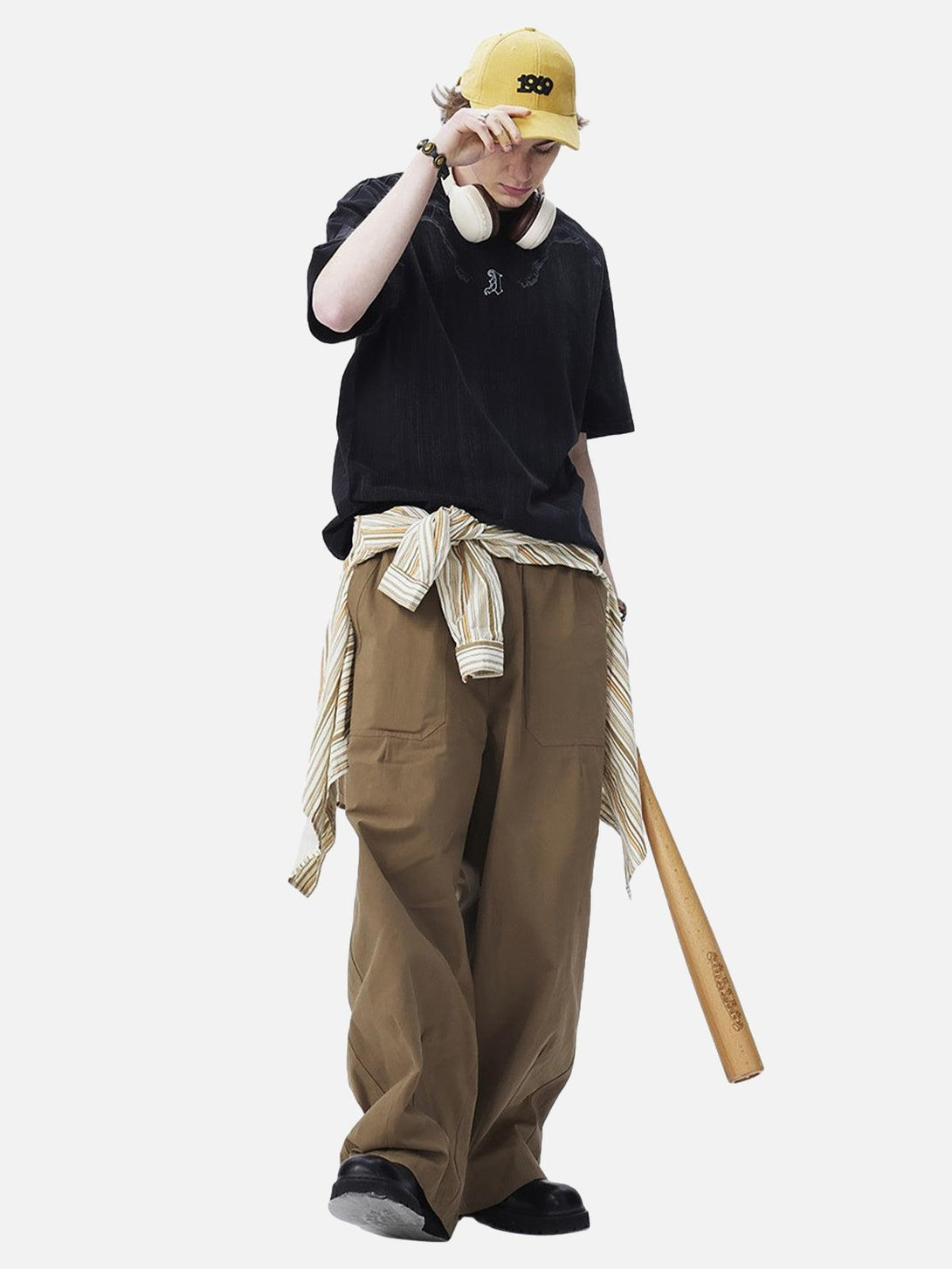 Model in a black TALISHKO embroidered T-shirt, khaki pants, yellow cap, and headphones.