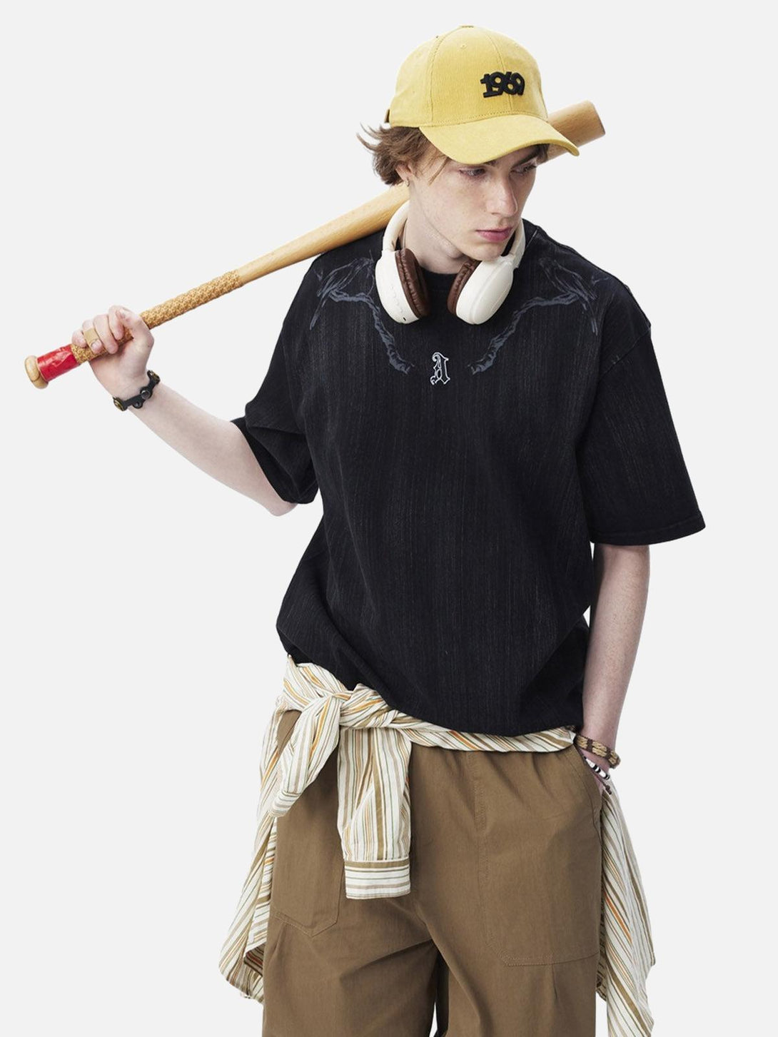 Model wearing a black embroidered T-shirt by TALISHKO, paired with khaki pants and a yellow cap.