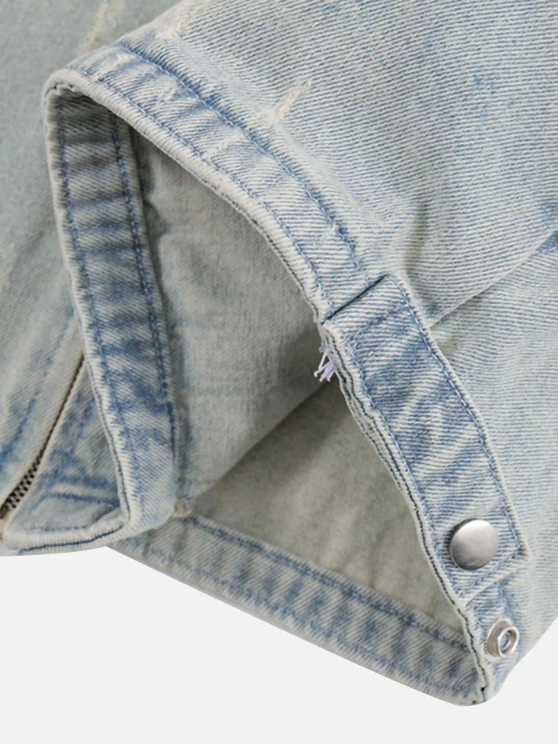 Focusing on the cuff and button detail of a TALISHKO denim jacket, showcasing frayed edges.