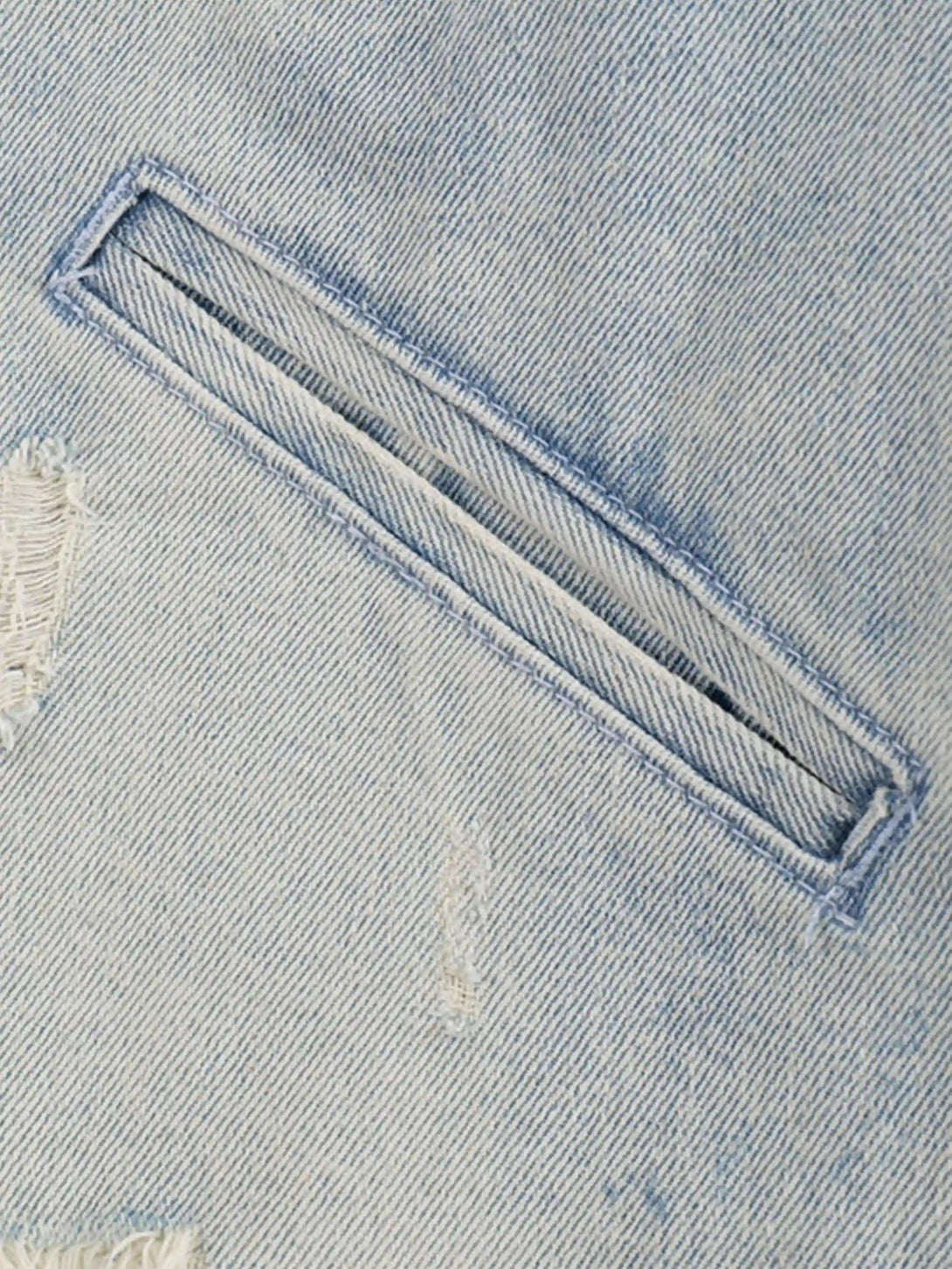 A tight crop highlighting the distressed pocket detail of a TALISHKO denim jacket.