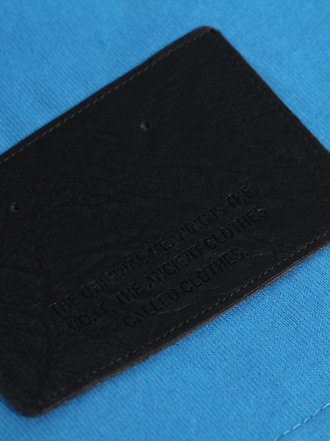 A close-up of TALISHKO's blue T-shirt, highlighting the textured black patch detail.