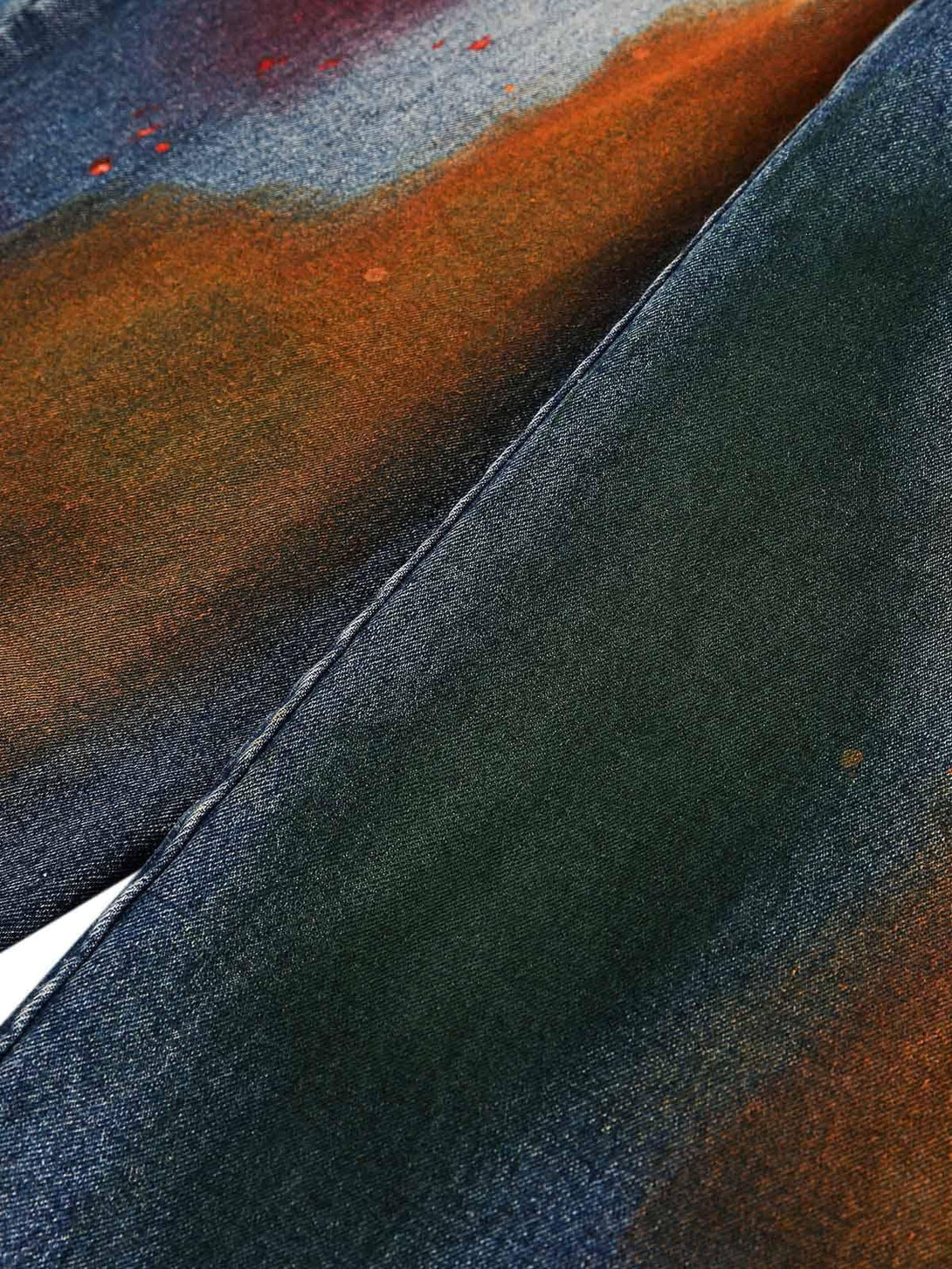 Zoomed-in texture of TALISHKO jeans, showcasing vibrant ink graffiti on denim fabric.