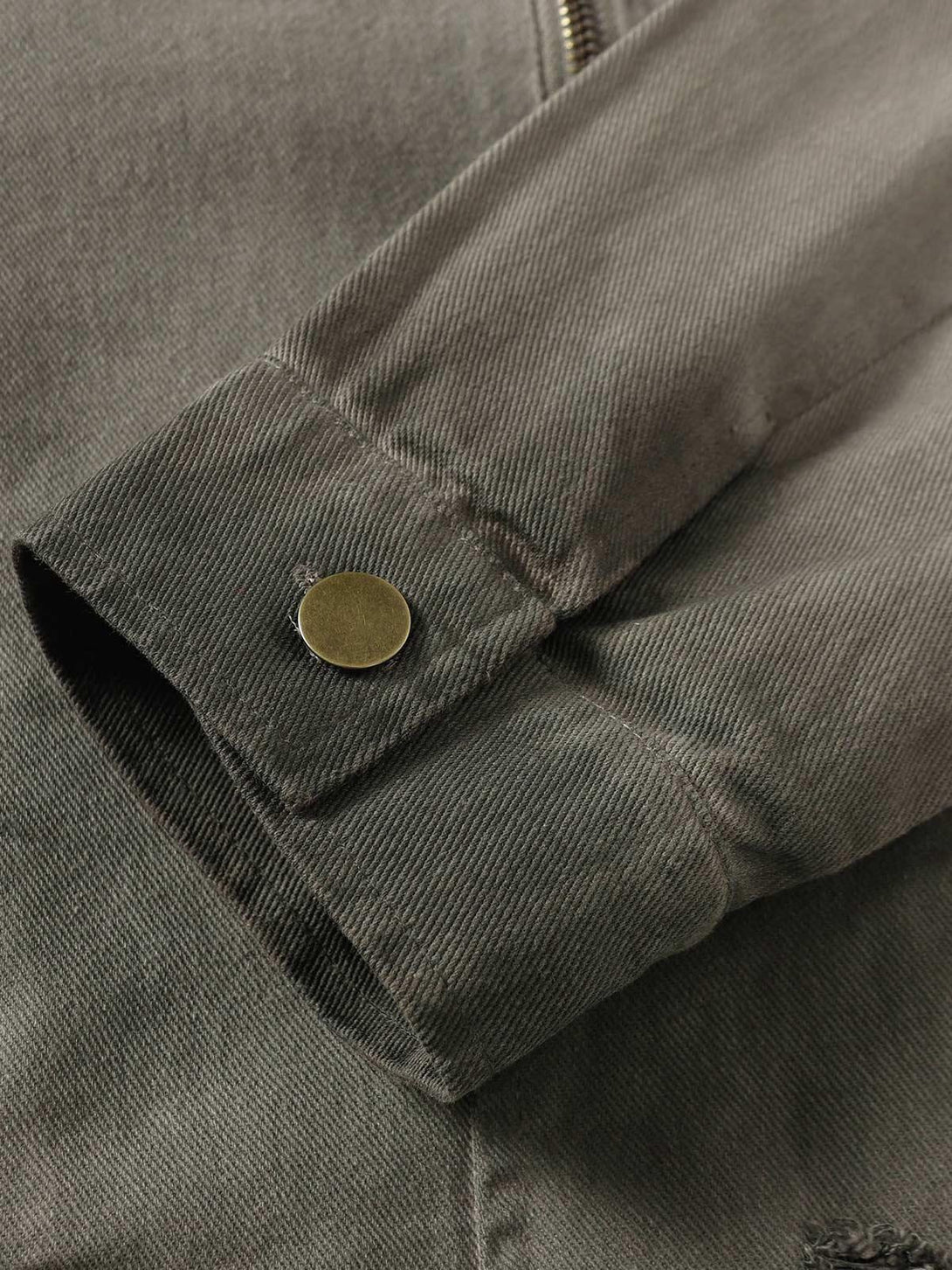 Focusing on the cuff detail of a TALISHKO denim jacket with a distressed texture and snap button.