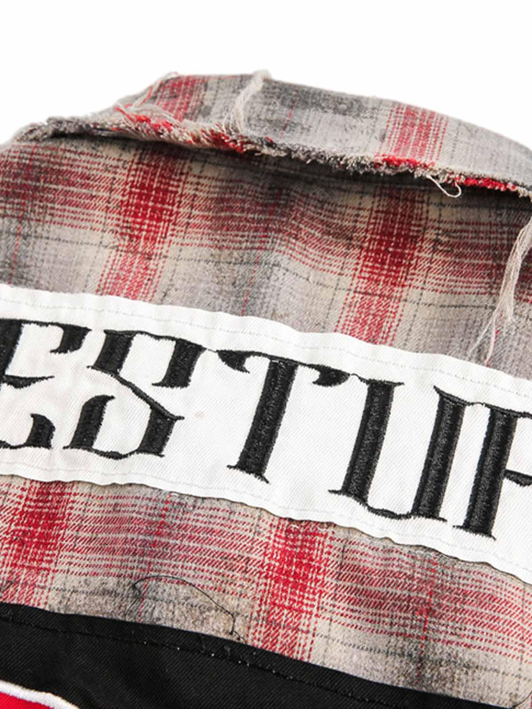 A detailed view of the distressed plaid fabric and bold patch design on a TALISHKO shirt.