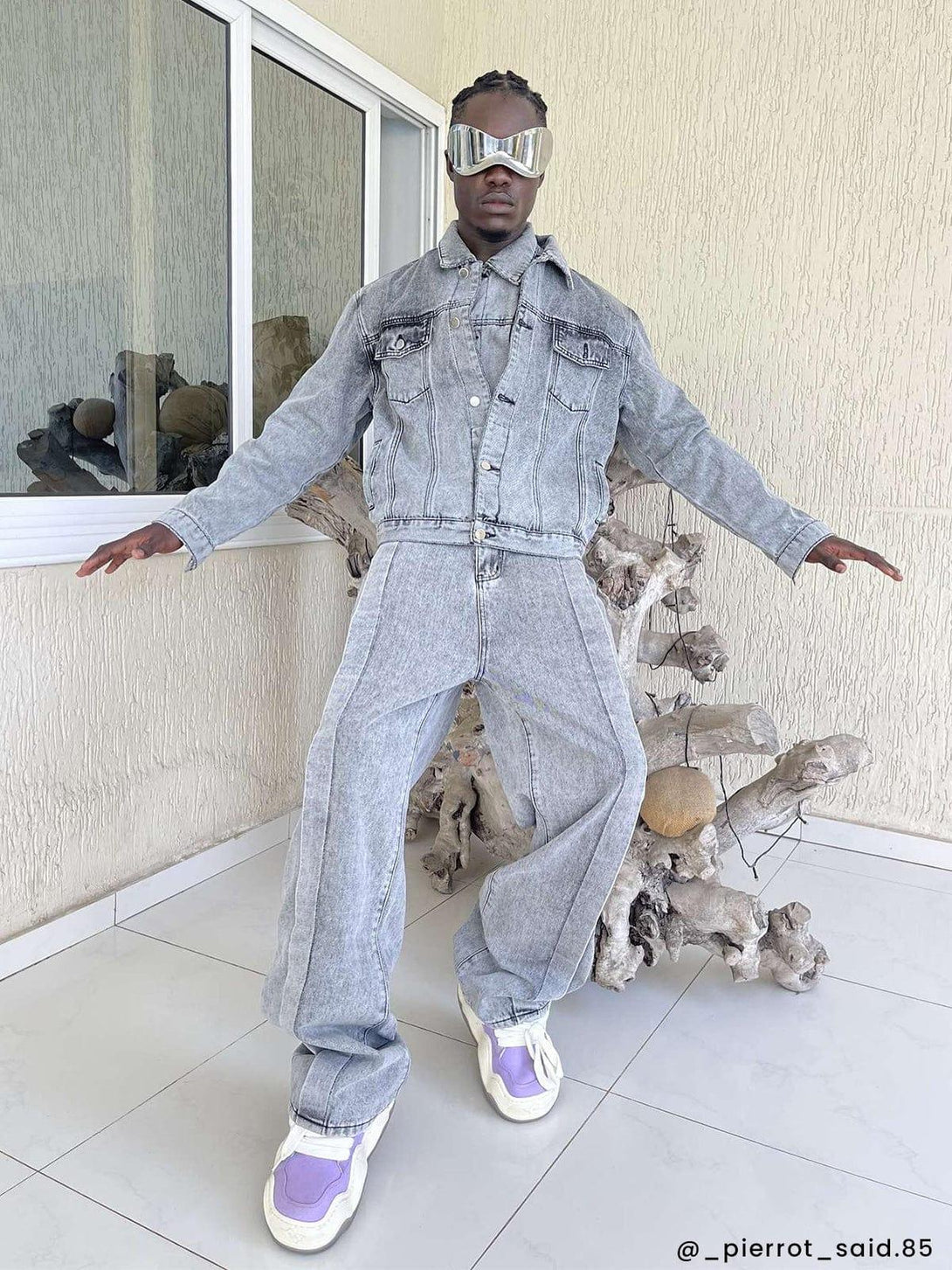 Model wearing gray denim jacket and jeans by TALISHKO, paired with futuristic sunglasses.