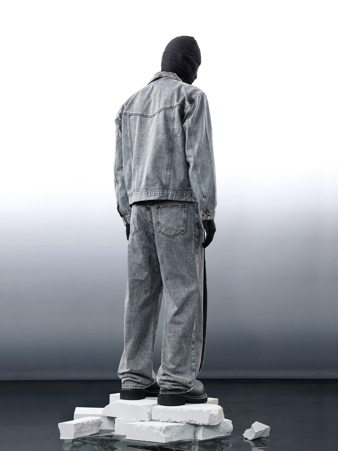 Back view of gray denim jacket and jeans by TALISHKO, styled with black mask and gloves.