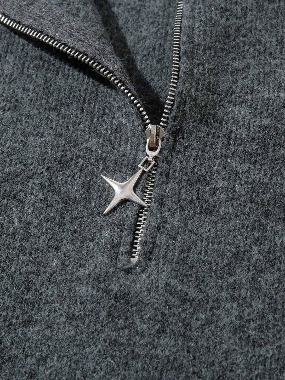 A close-up of the star-shaped zipper pull on a distressed sweater by TALISHKO.