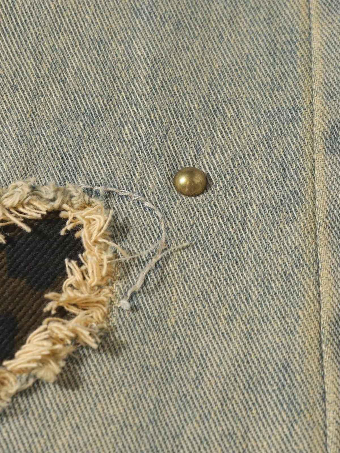 Intricate look at TALISHKO distressed jeans, highlighting raw edge patch and textured fabric.