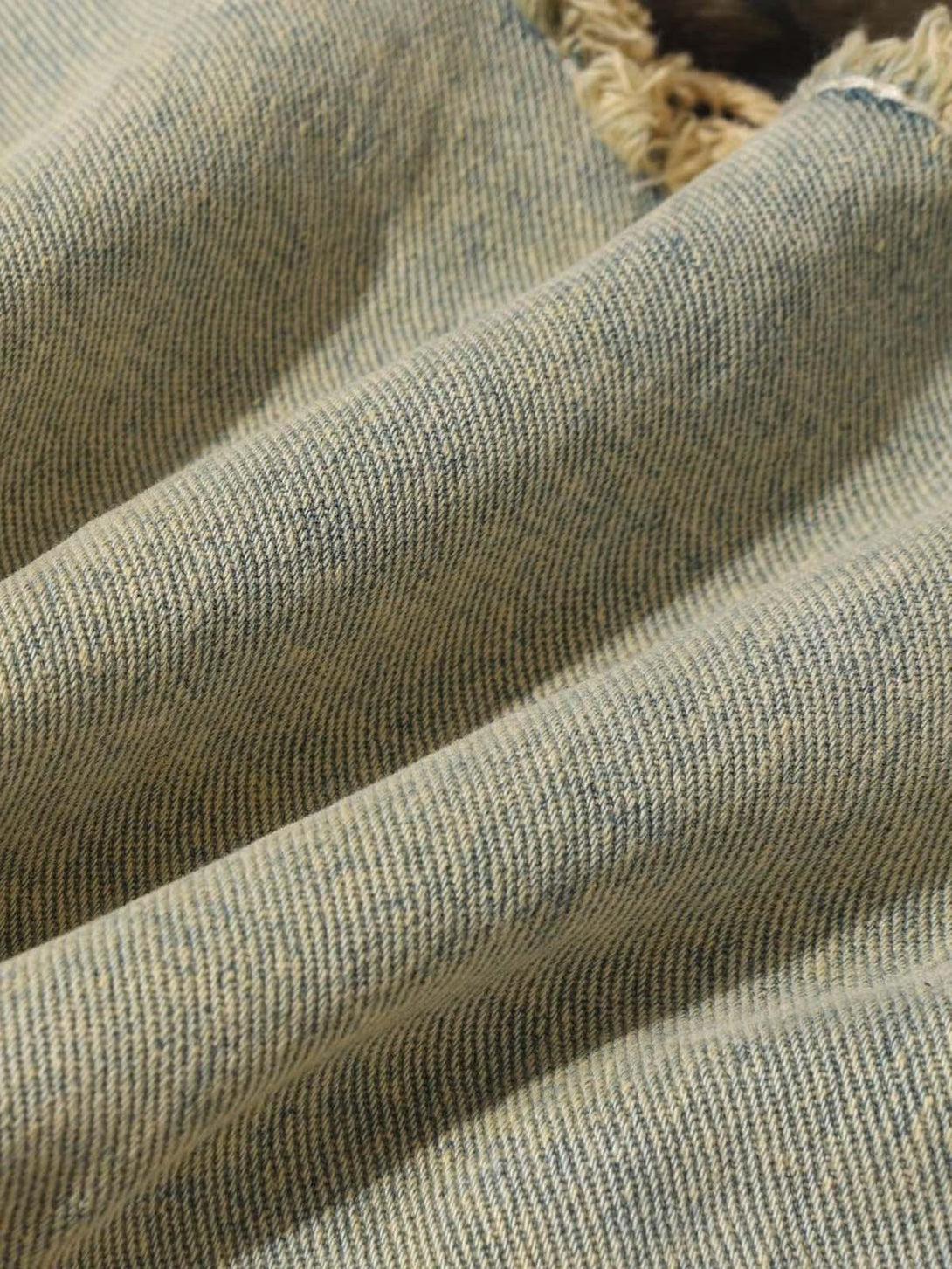 Zoomed-in texture of TALISHKO distressed jeans, highlighting the raw edge detail and fabric weave.