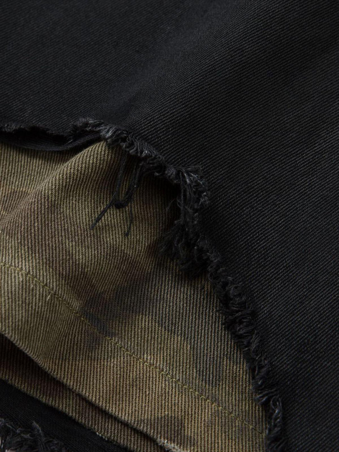 Detailed fabric and stitching of TALISHKO black denim shorts with distressed rips and camo lining.