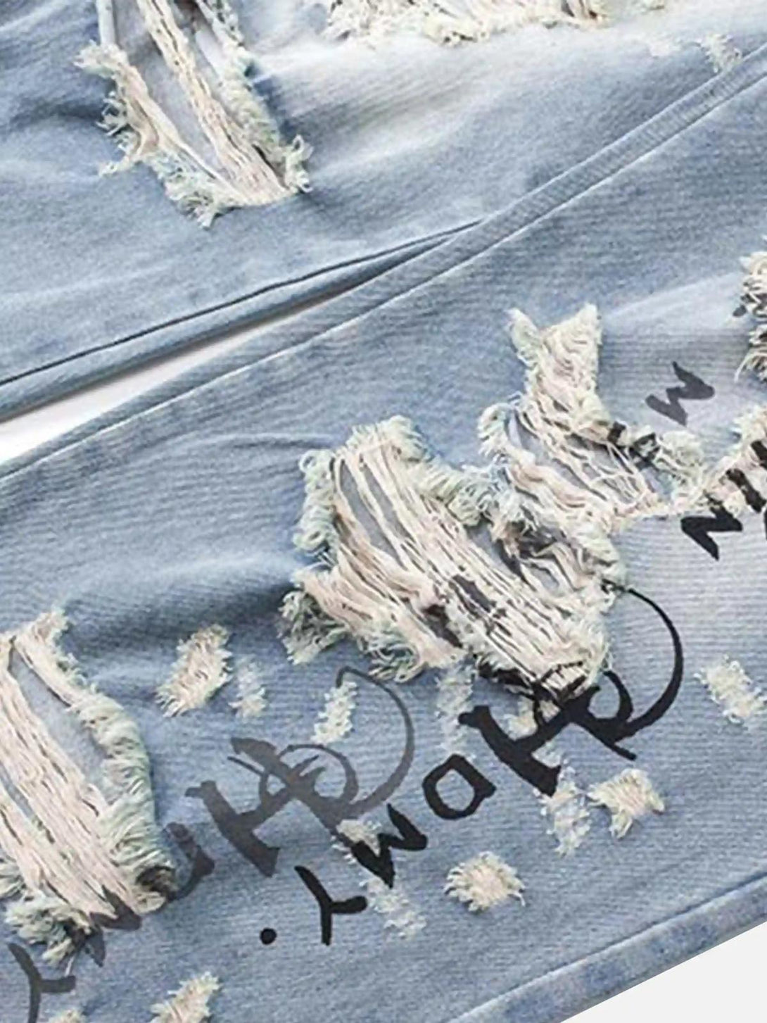 A close-up of TALISHKO jeans highlighting distressed texture and unique letter print design.