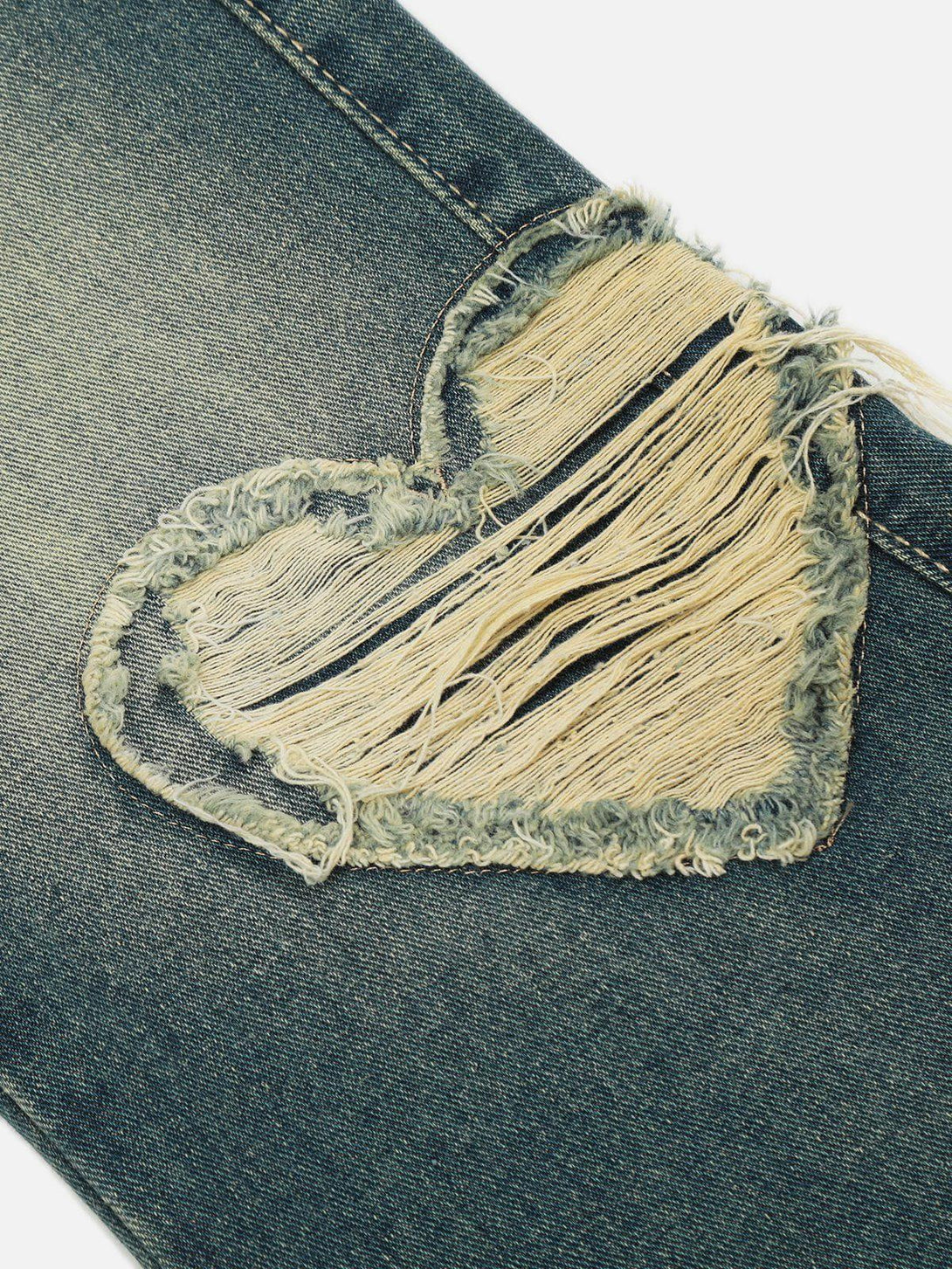 A close-up of TALISHKO jeans showcasing a distressed heart patch with fringed edges.