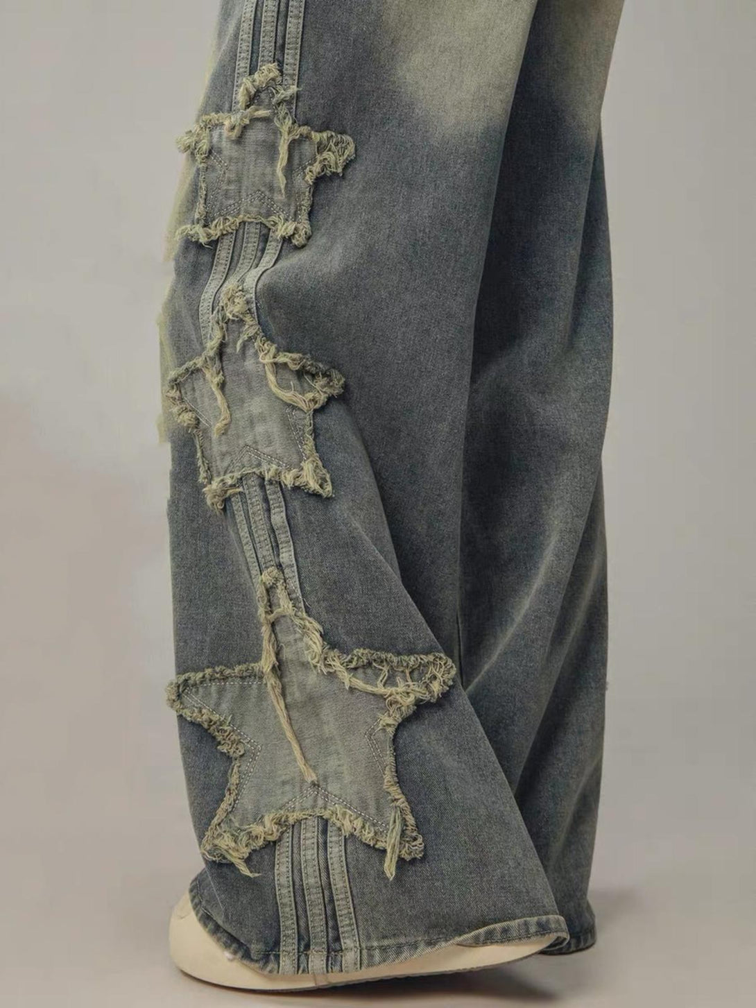 Focusing on the frayed star patches and texture of TALISHKO distressed jeans, side view.