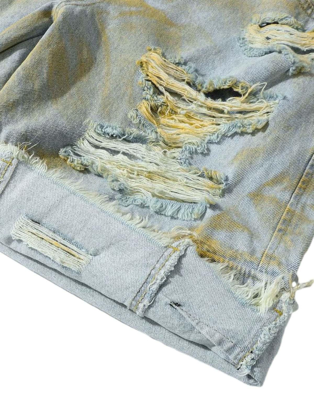 A close-up of TALISHKO distressed tie-dye denim shorts, highlighting frayed and rugged texture.