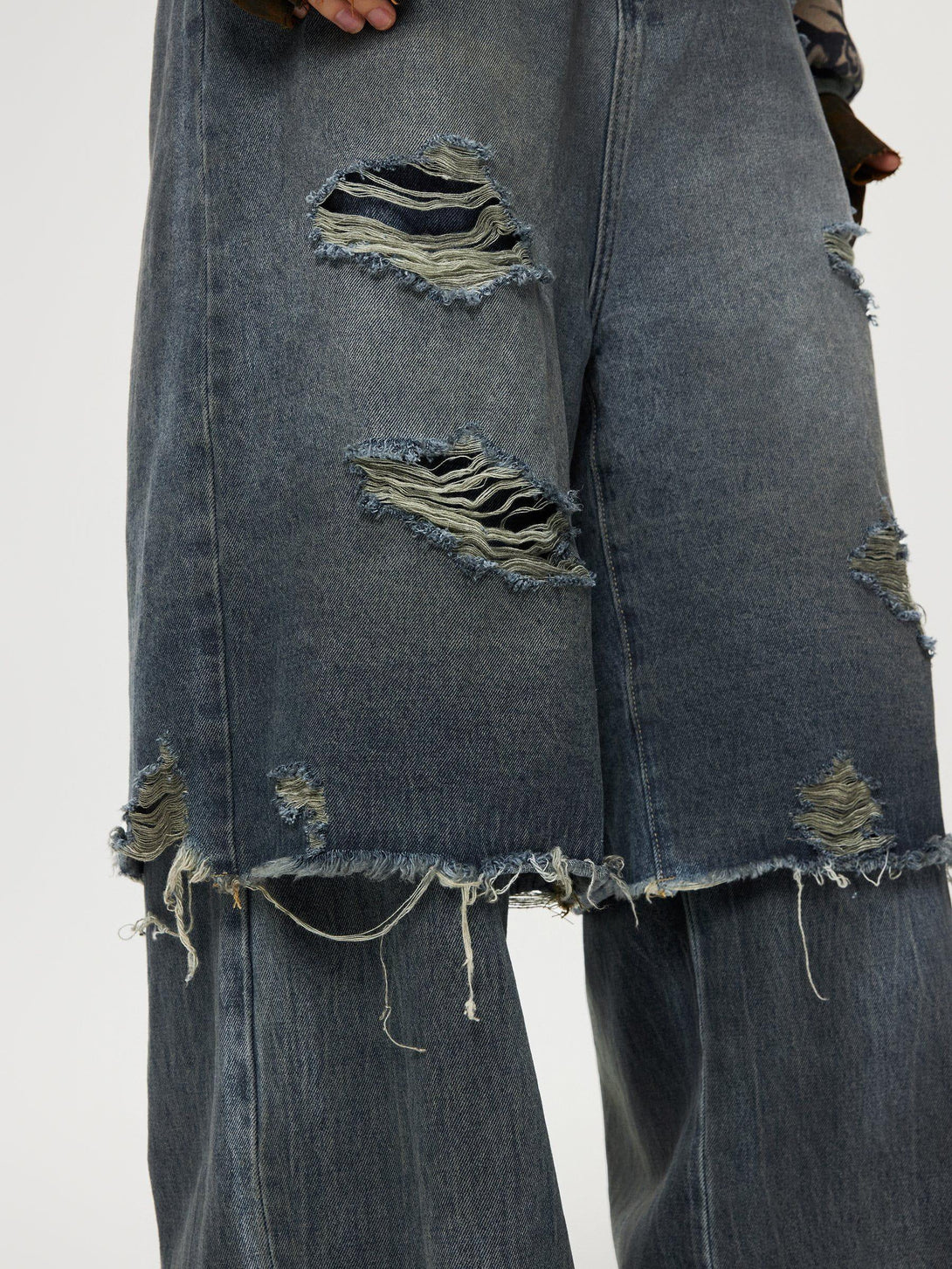 A close-up of TALISHKO distressed baggy jeans, showcasing frayed details and layered design.