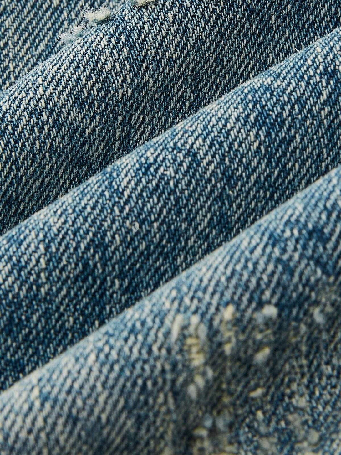Zoomed-in texture of TALISHKO's distressed denim, highlighting the unique washed finish.