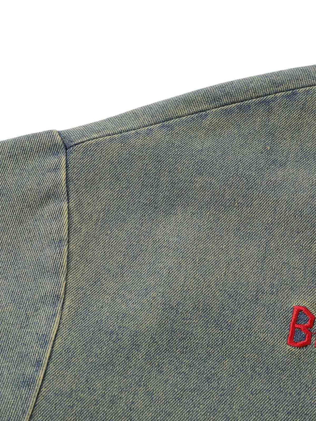 Zoomed-in texture of TALISHKO's distressed denim T-shirt, highlighting intricate stitching.