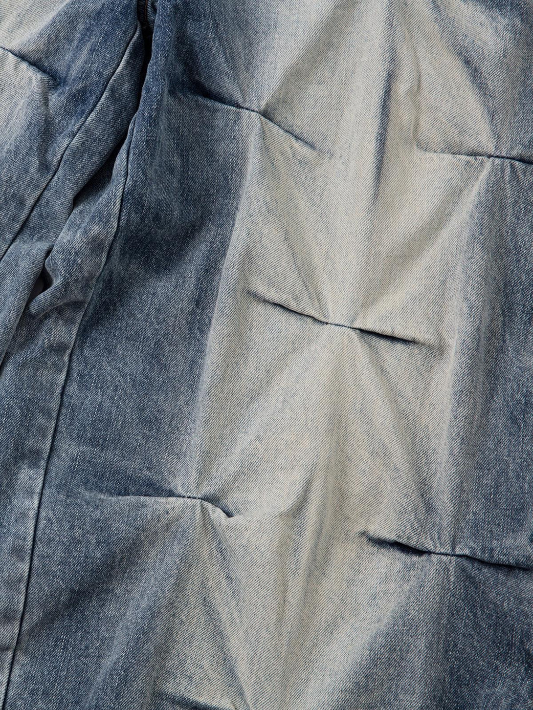 A tight crop highlighting the distressed texture of TALISHKO's washed pleated jeans.