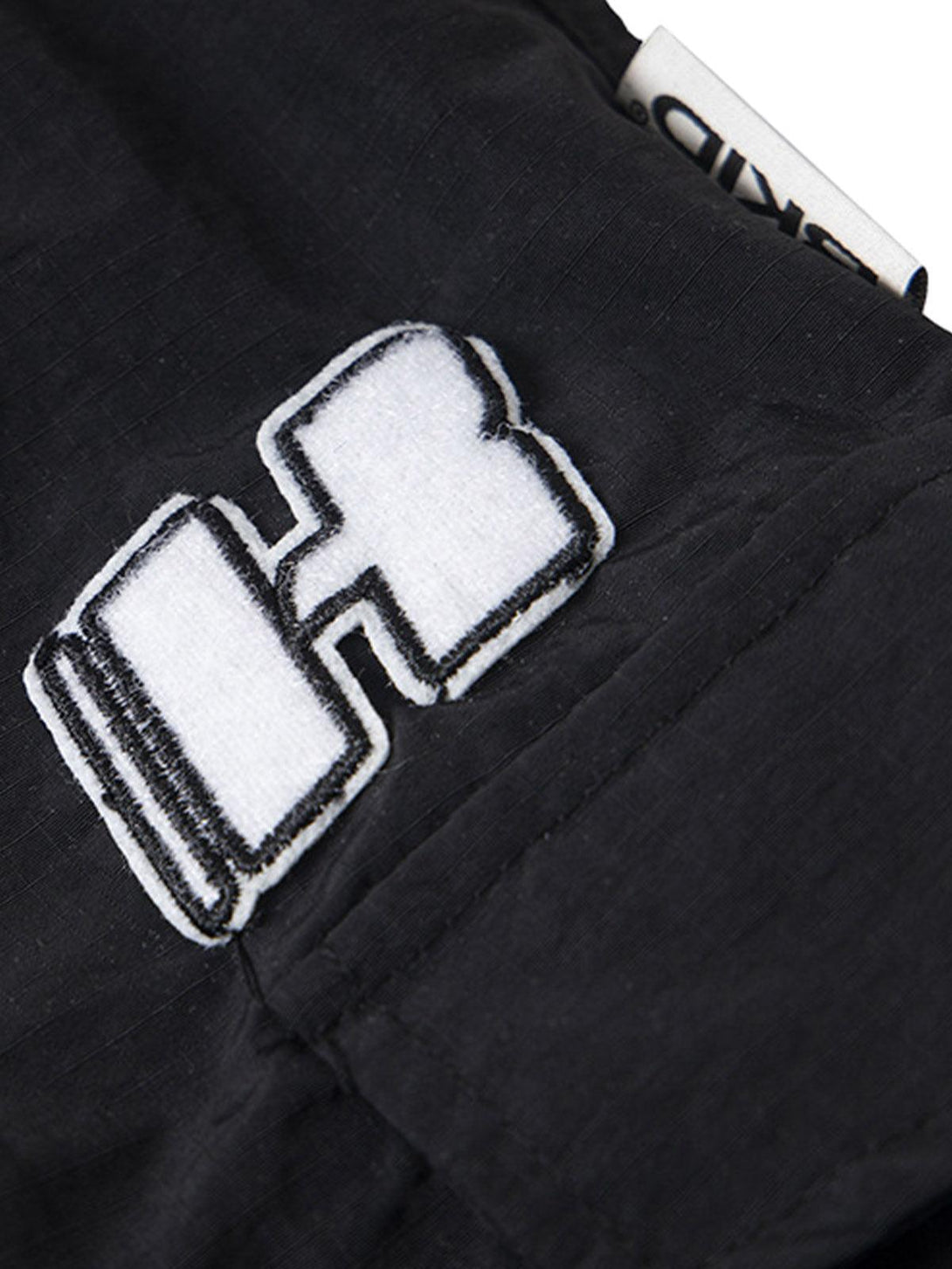 Focusing on the bold logo embroidery detail on black cargo pants by TALISHKO.