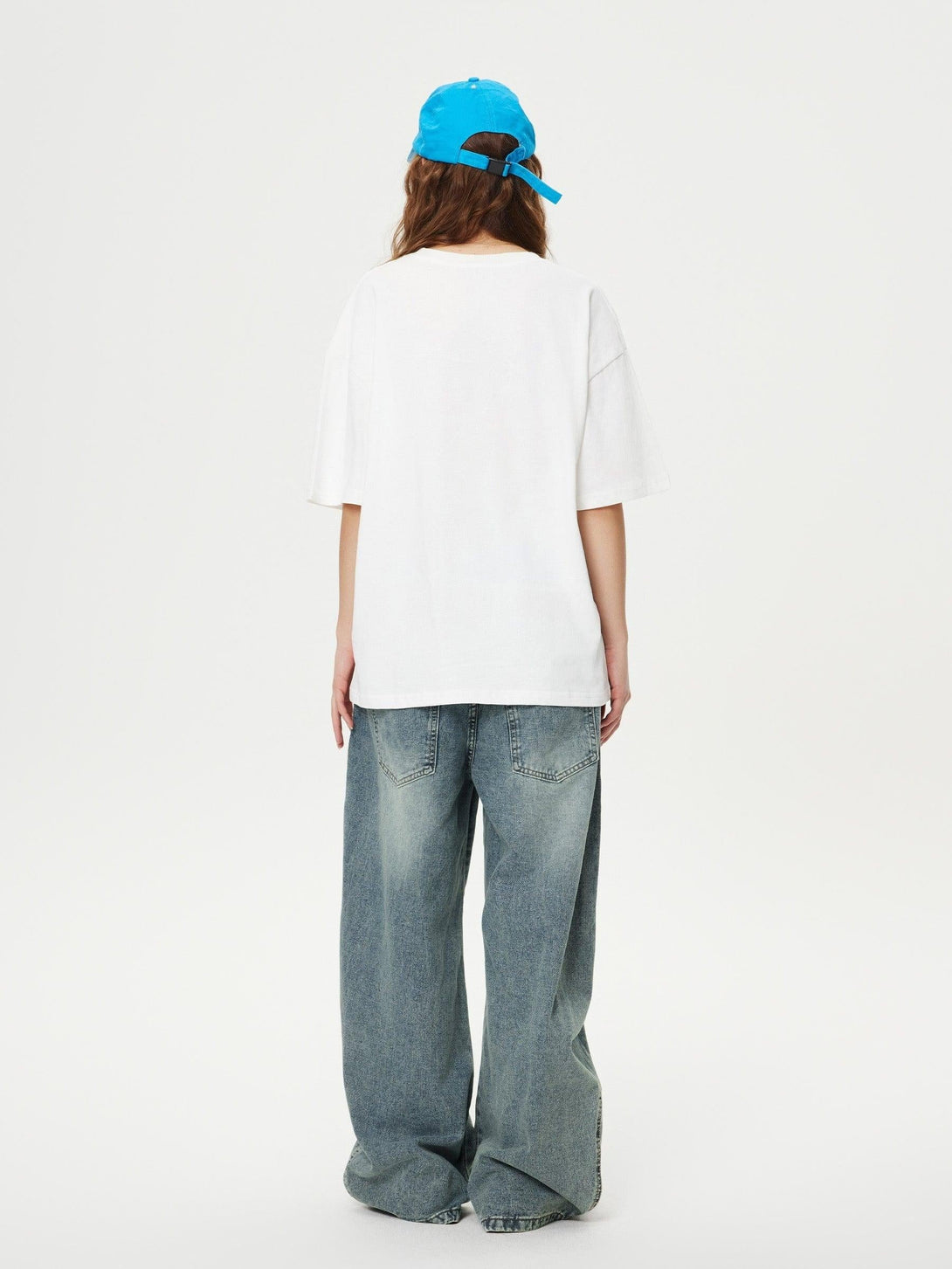 Model in TALISHKO loose jeans, white tee, and blue cap, viewed from behind for a casual look.
