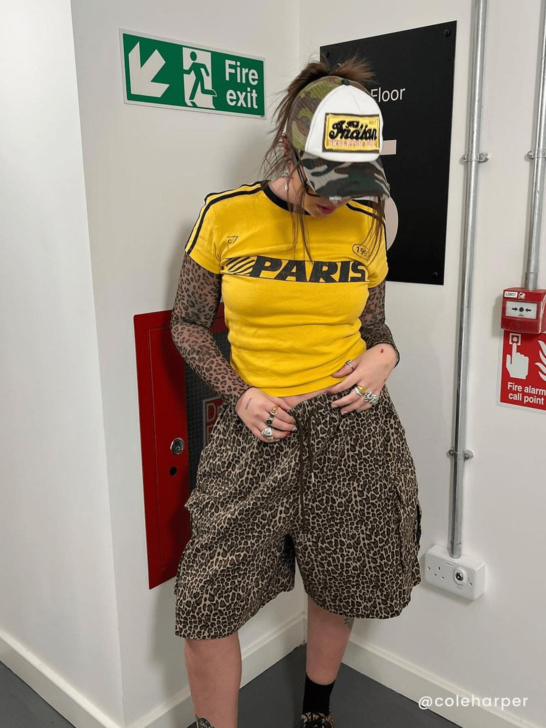 Model wearing leopard print shorts with a yellow "Paris" top and camo hat by TALISHKO.