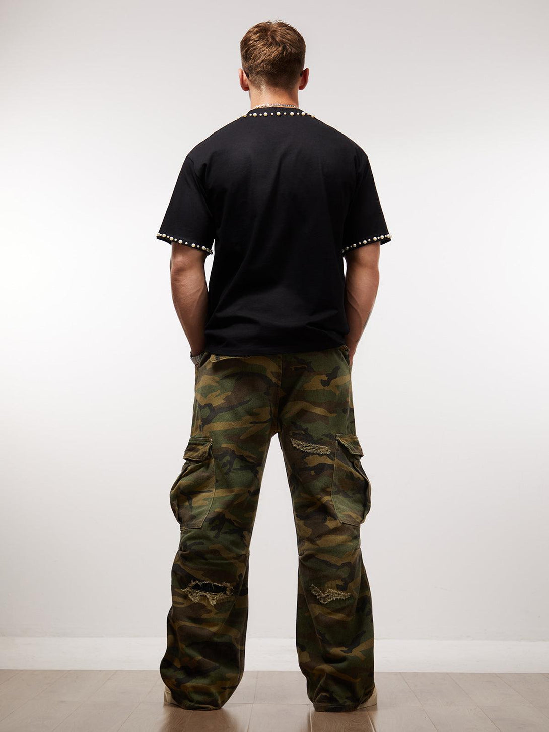 Back view of pearl-embellished black T-shirt by TALISHKO paired with camo cargo pants.