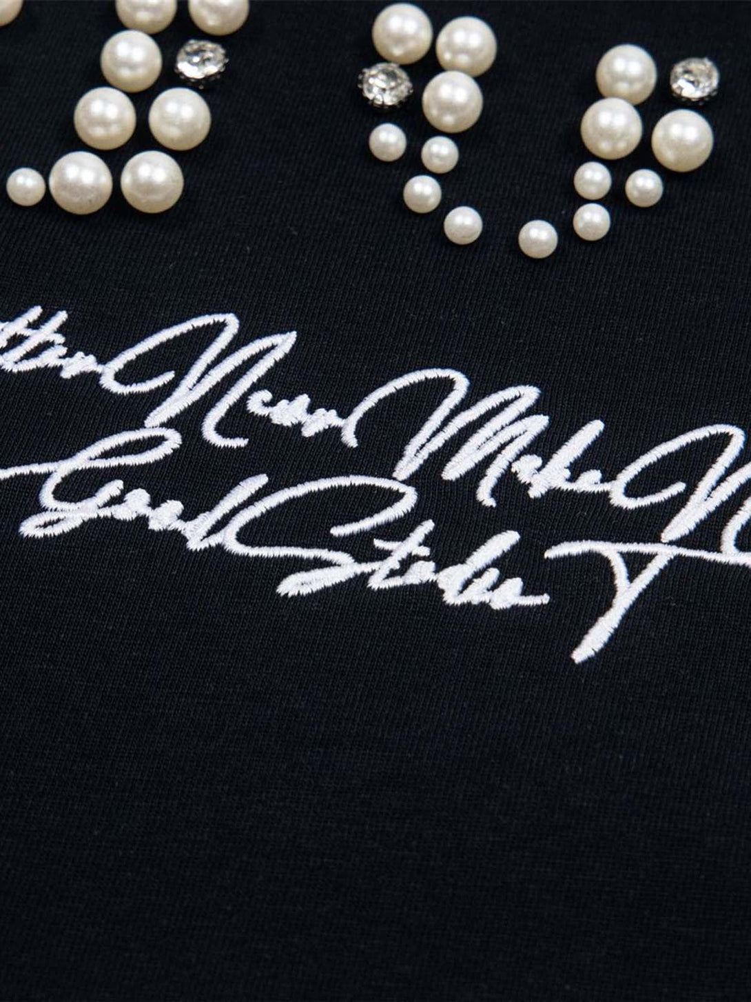 Intricate look at pearl embellishments on a black T-shirt by TALISHKO, highlighting elegant details.