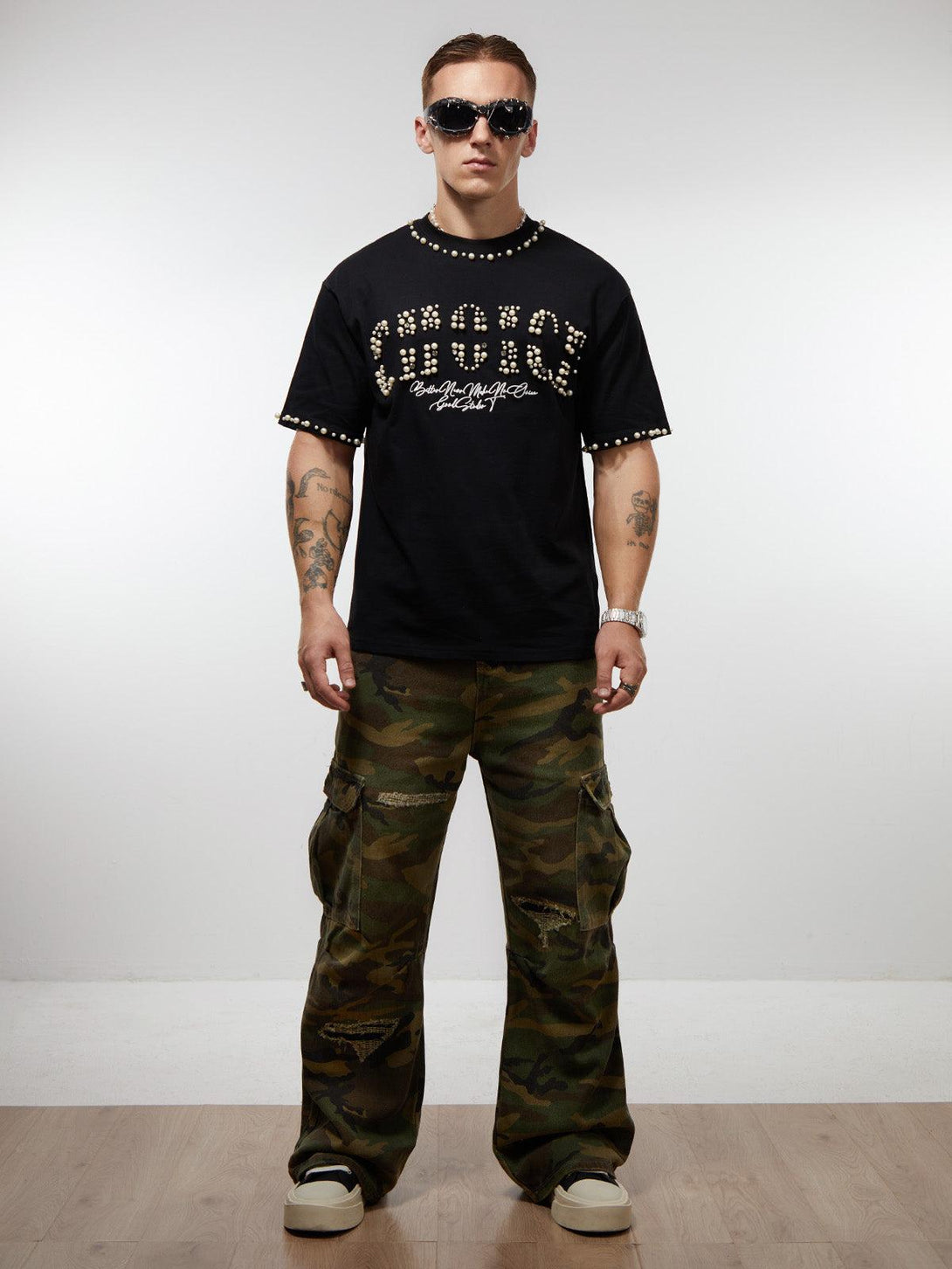 Model in camo cargo pants and pearl-embellished black T-shirt by TALISHKO, exuding urban style.