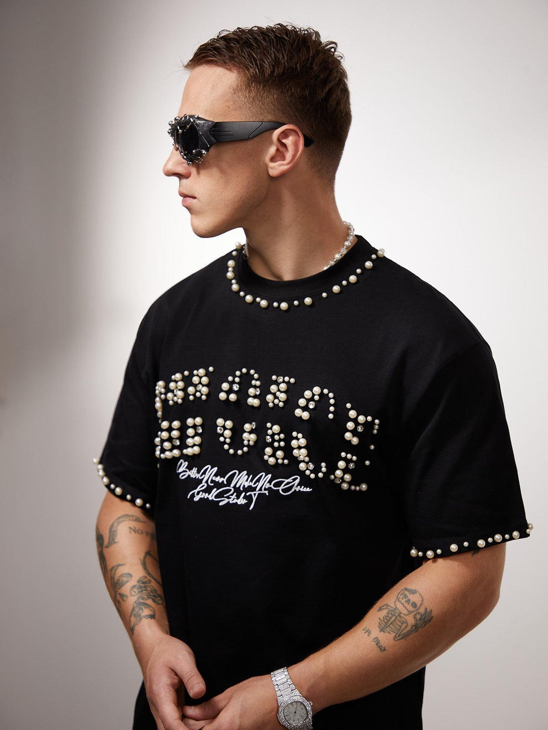 Model in a pearl-embellished black T-shirt by TALISHKO, wearing stylish sunglasses.
