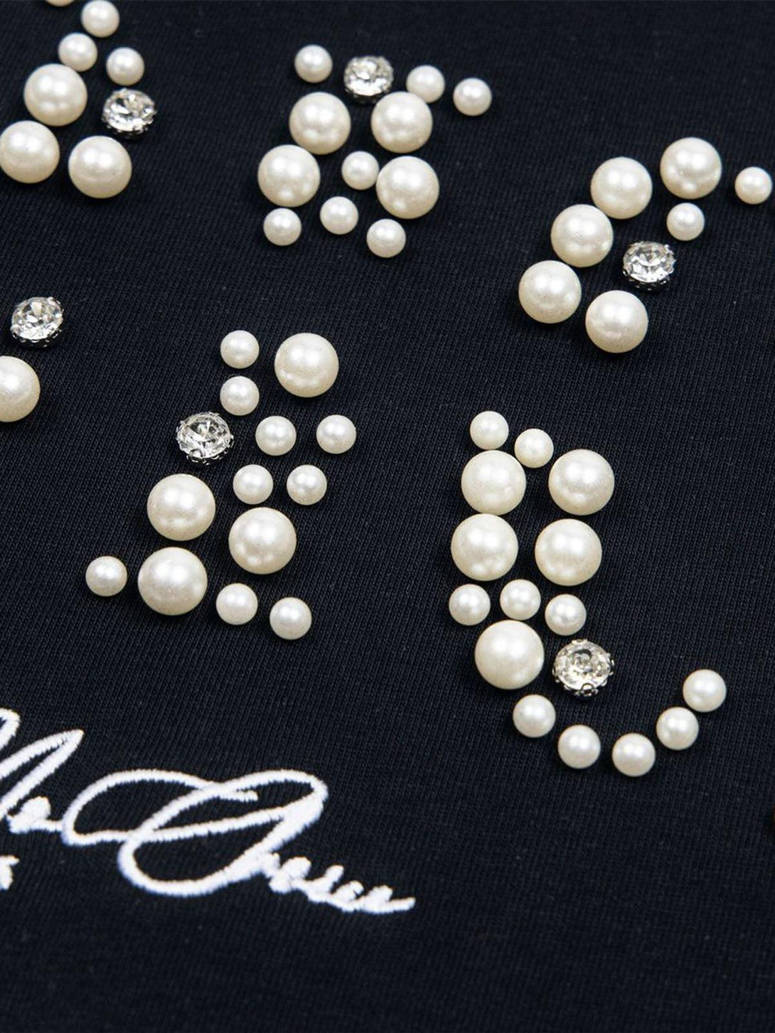 Focusing on the pearl and gem embellishments on TALISHKO's black oversized T-shirt, showcasing elegance.