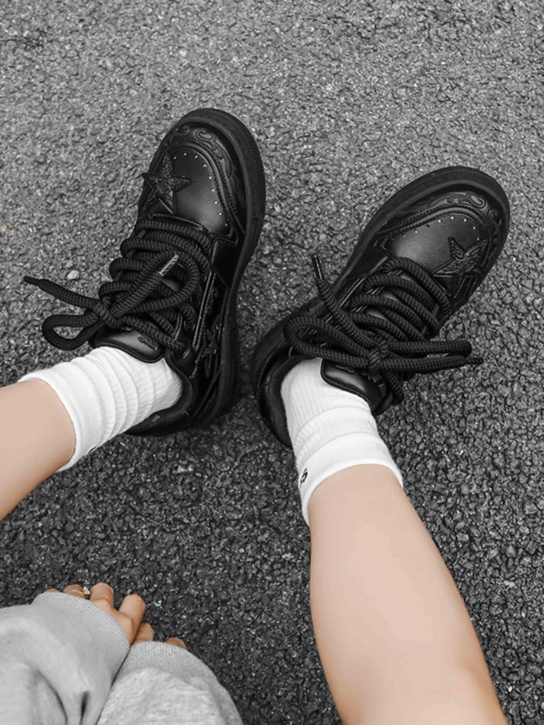 A pair of black embossed star board shoes by TALISHKO, worn with white socks on pavement.