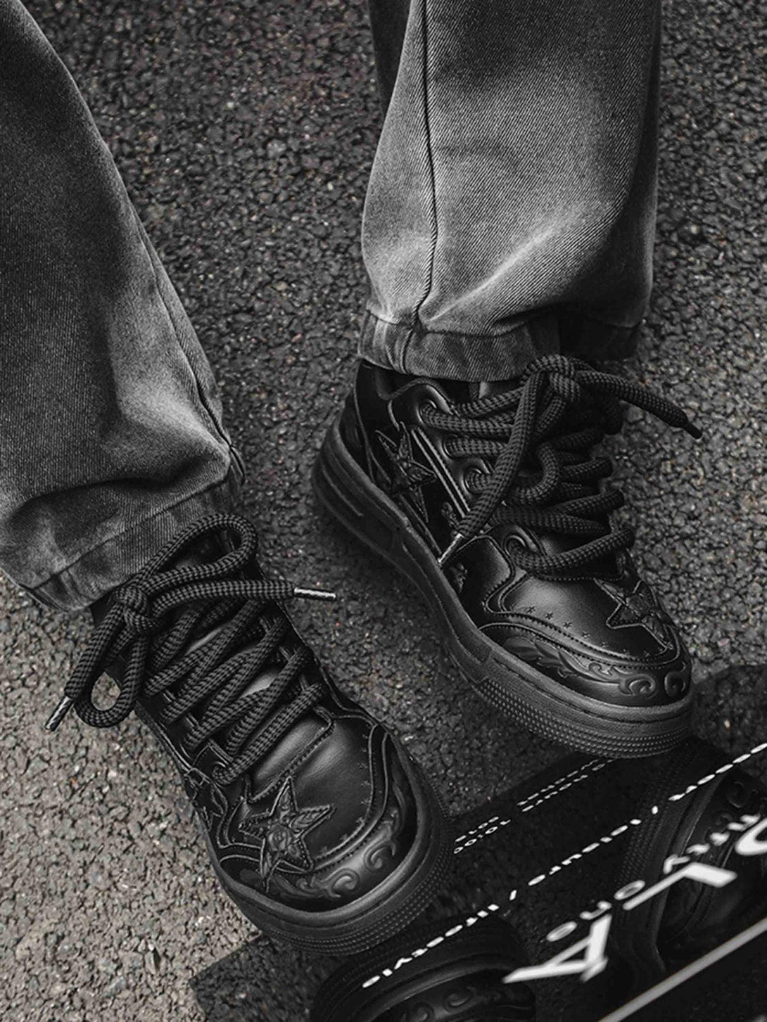 A stylish close-up of TALISHKO's black embossed star board shoes paired with dark jeans.