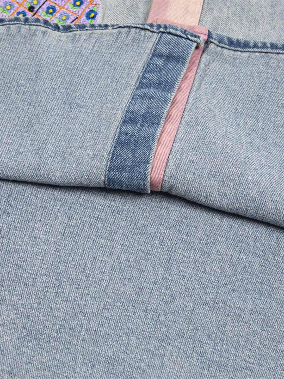 Zoomed-in texture of TALISHKO's denim shirt, showcasing pink accents and embroidered details.