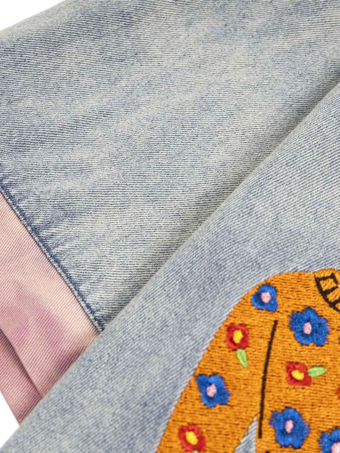 Intricate design detail from TALISHKO's denim shirt, highlighting colorful embroidery and pink accents.