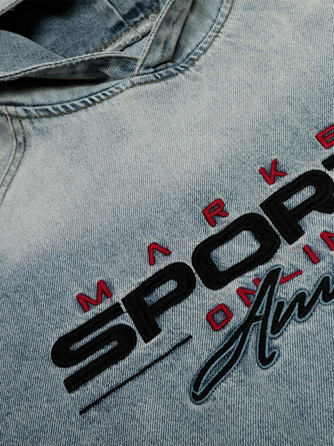 Detailed view of embroidered text on a washed denim hoodie by TALISHKO, highlighting texture.