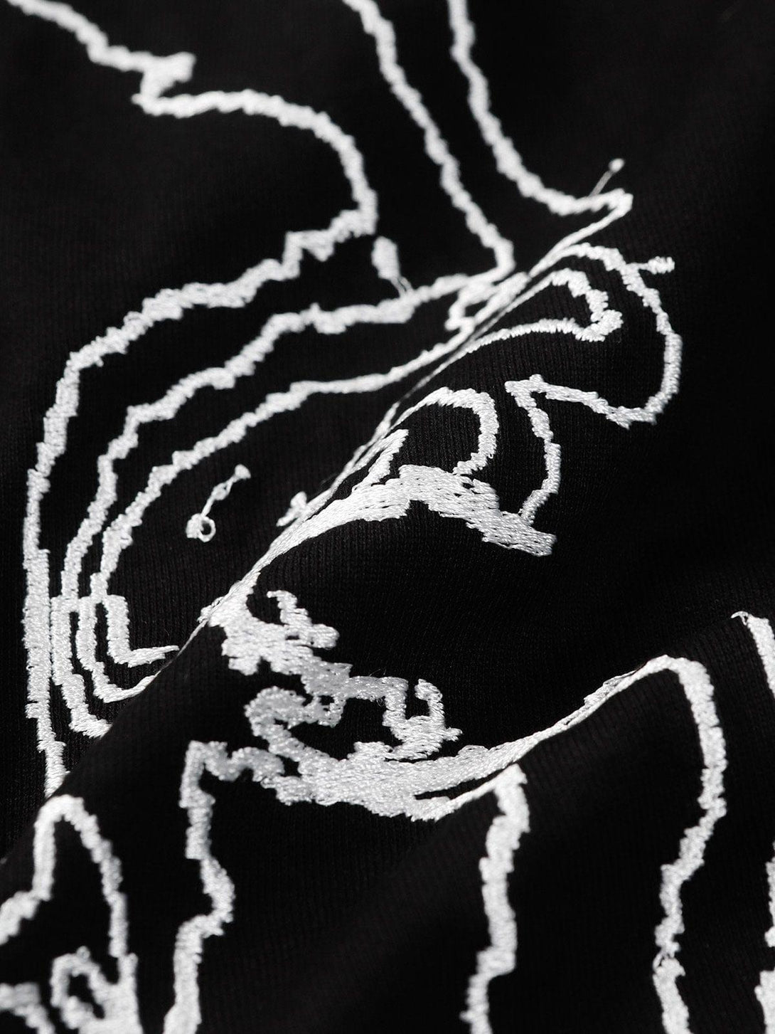 Intricate embroidery detail on TALISHKO tee showcasing an abstract face design on black fabric.