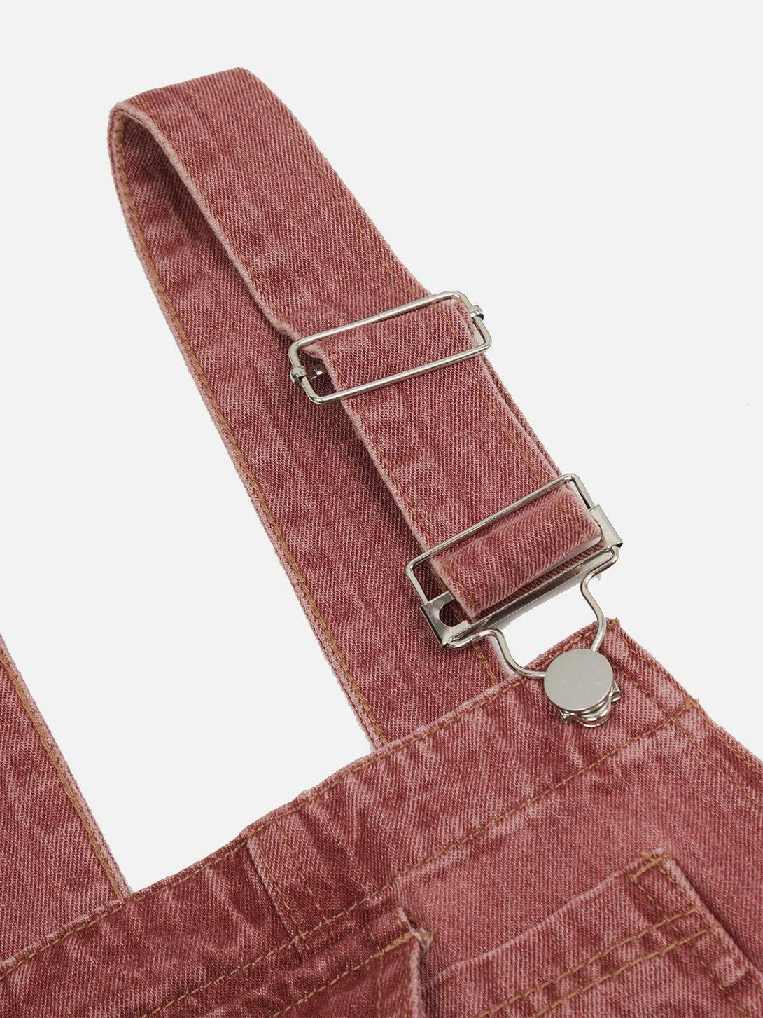 A close-up of the adjustable strap on TALISHKO's washed pink overalls, highlighting the denim texture.