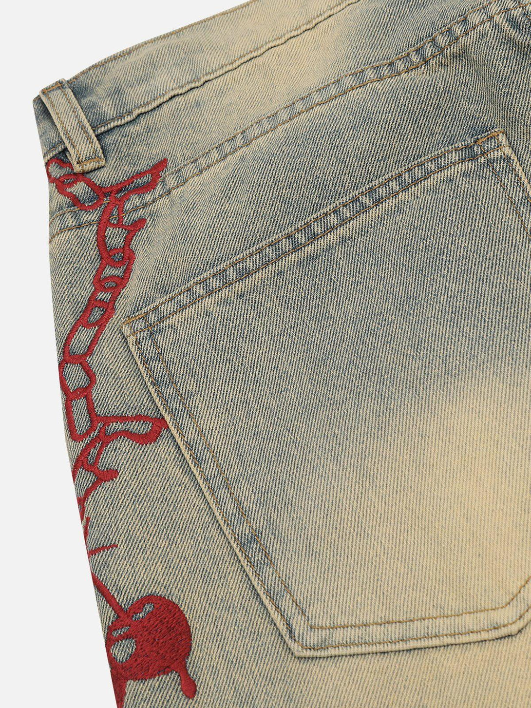 Detailed view of TALISHKO jeans, highlighting red embroidery on washed denim fabric.