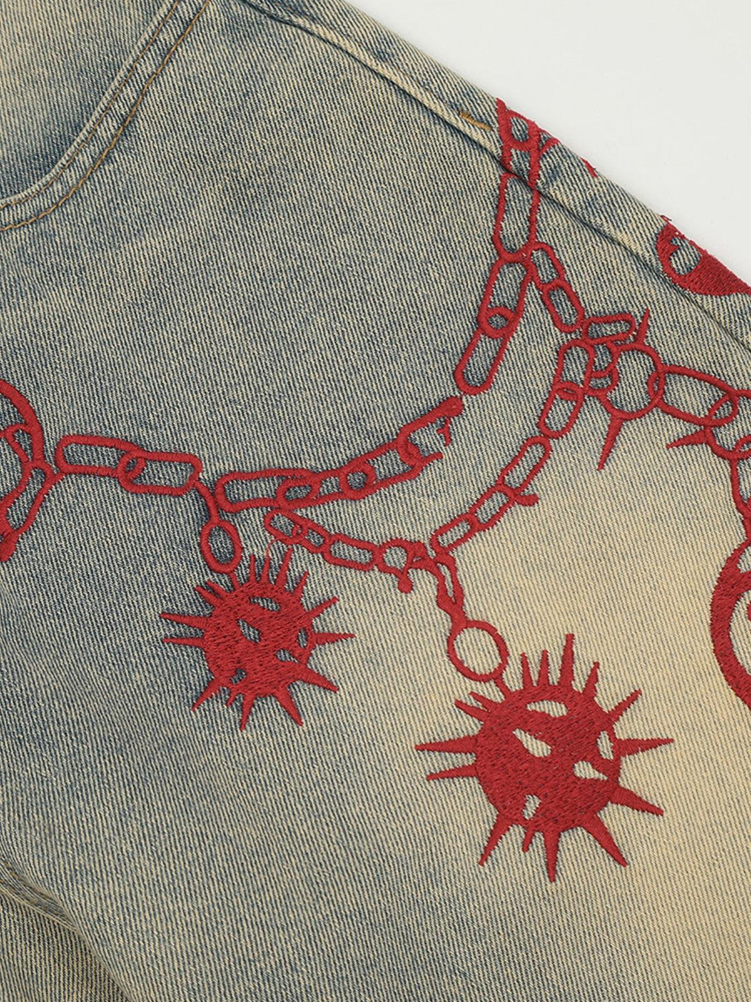 Intricate look at TALISHKO jeans with bold red embroidery on washed denim, adding artistic flair.