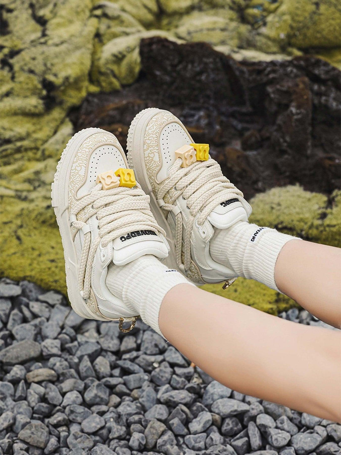 TALISHKO sneakers in cream with unique patterns, styled with casual white socks on gravel.
