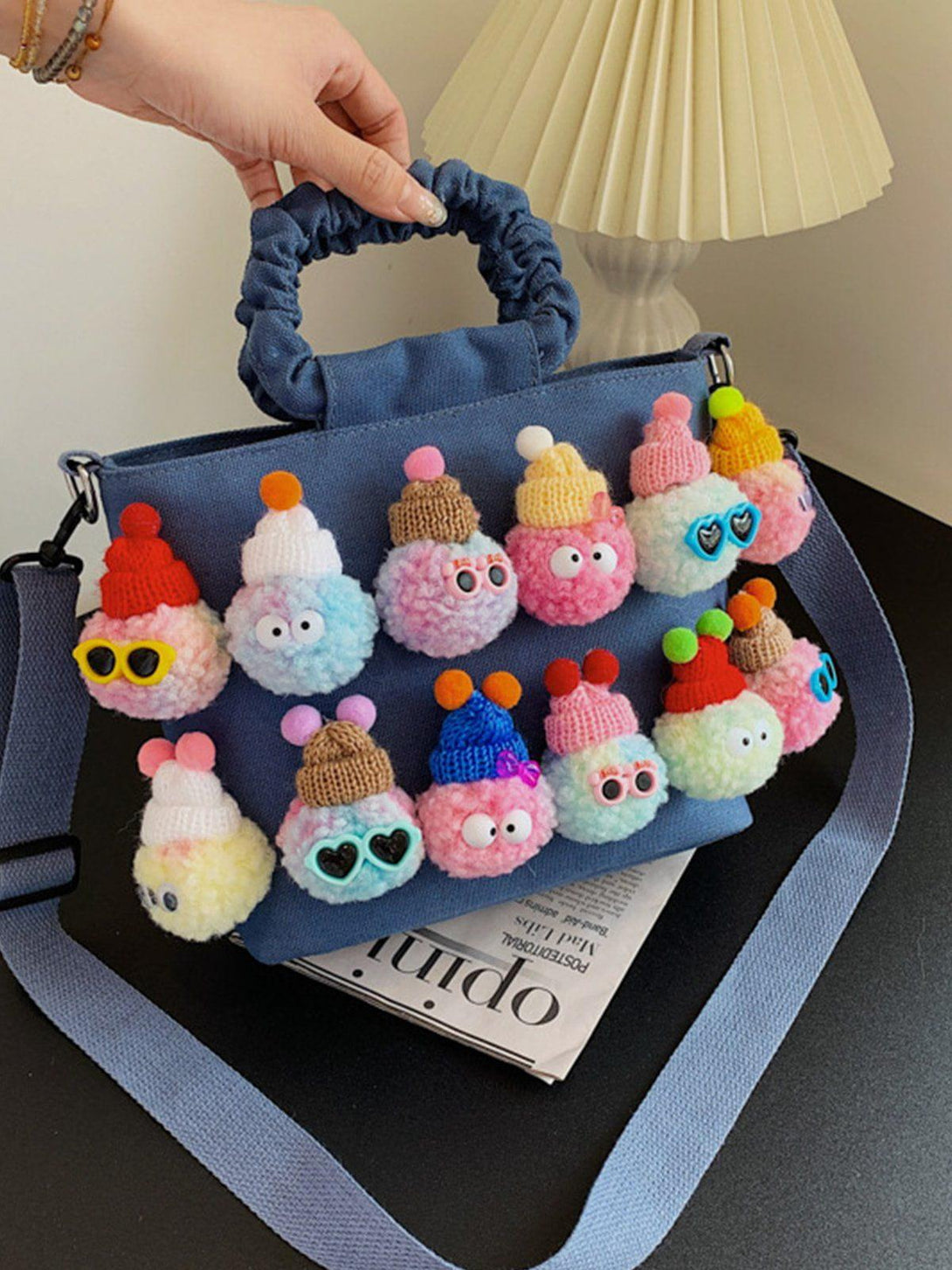 TALISHKO's canvas bag features playful pom-pom characters, adding whimsy to any ensemble.