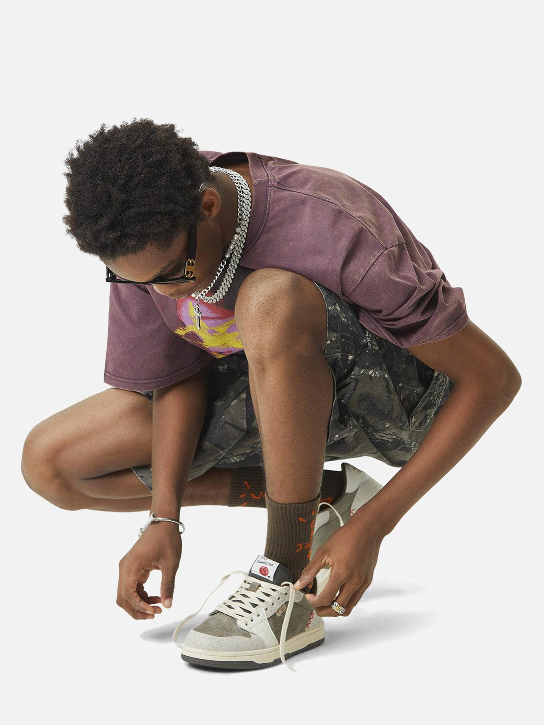 Model tying sneakers while wearing TALISHKO camouflage shorts, highlighting urban street style.