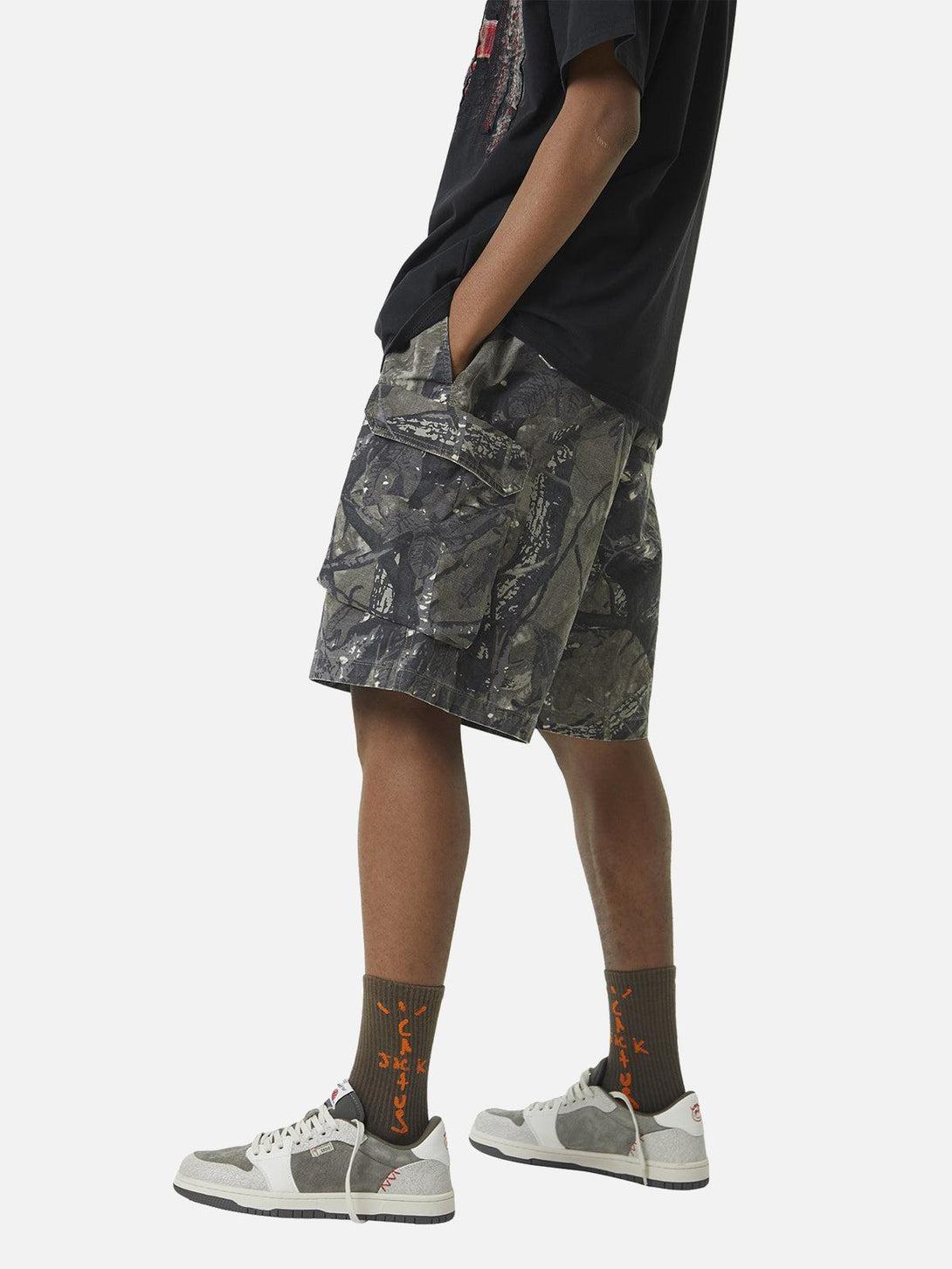 Model in TALISHKO camouflage shorts with graphic tee, highlighting casual streetwear vibe.