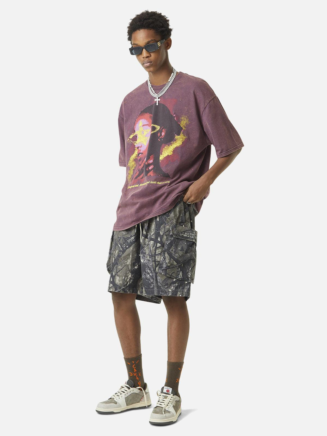 Model in TALISHKO graphic tee and camouflage shorts, showcasing urban streetwear style.