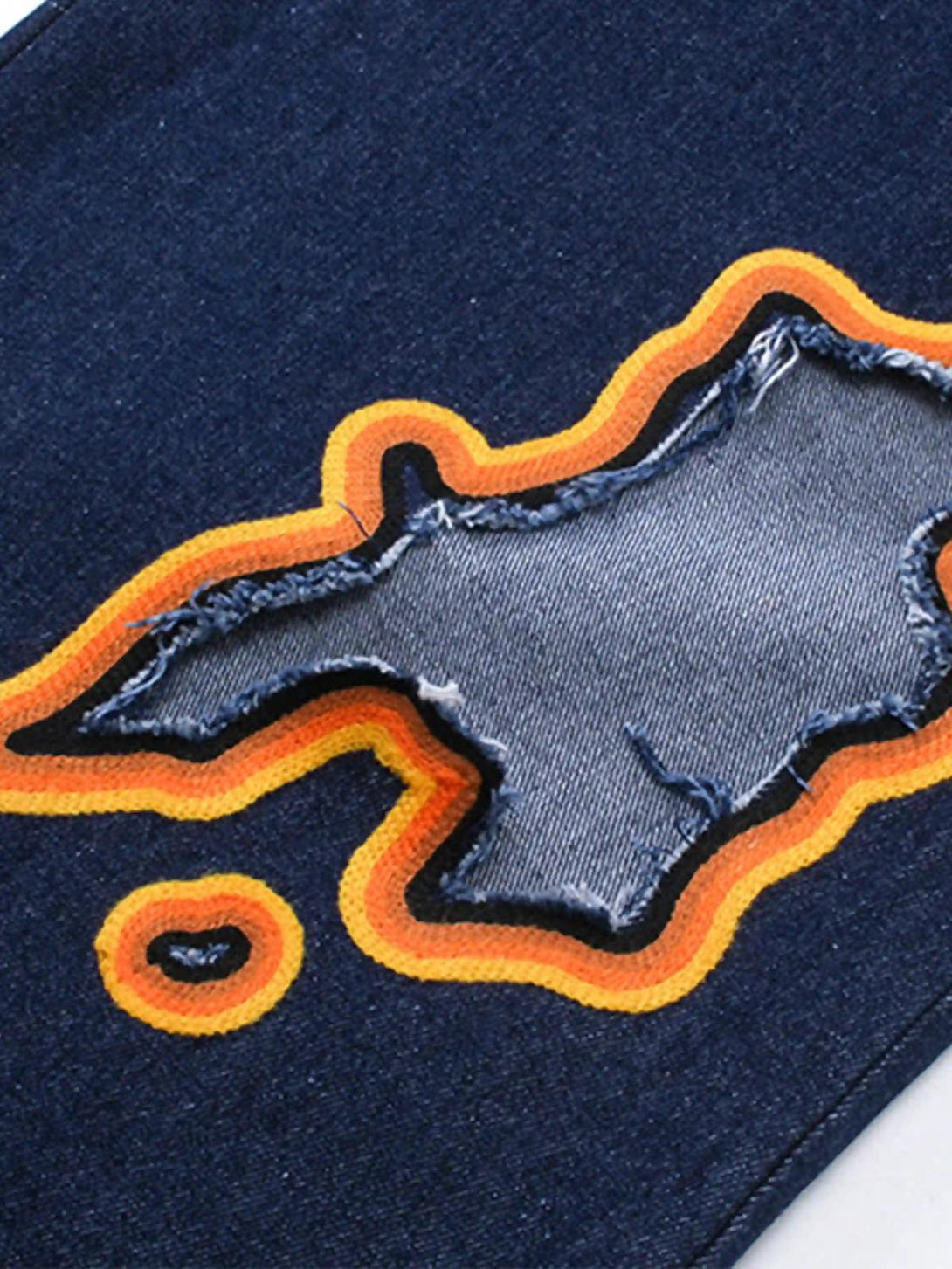 A detailed view of TALISHKO's flame-scarred embroidery on denim, highlighting unique textures.