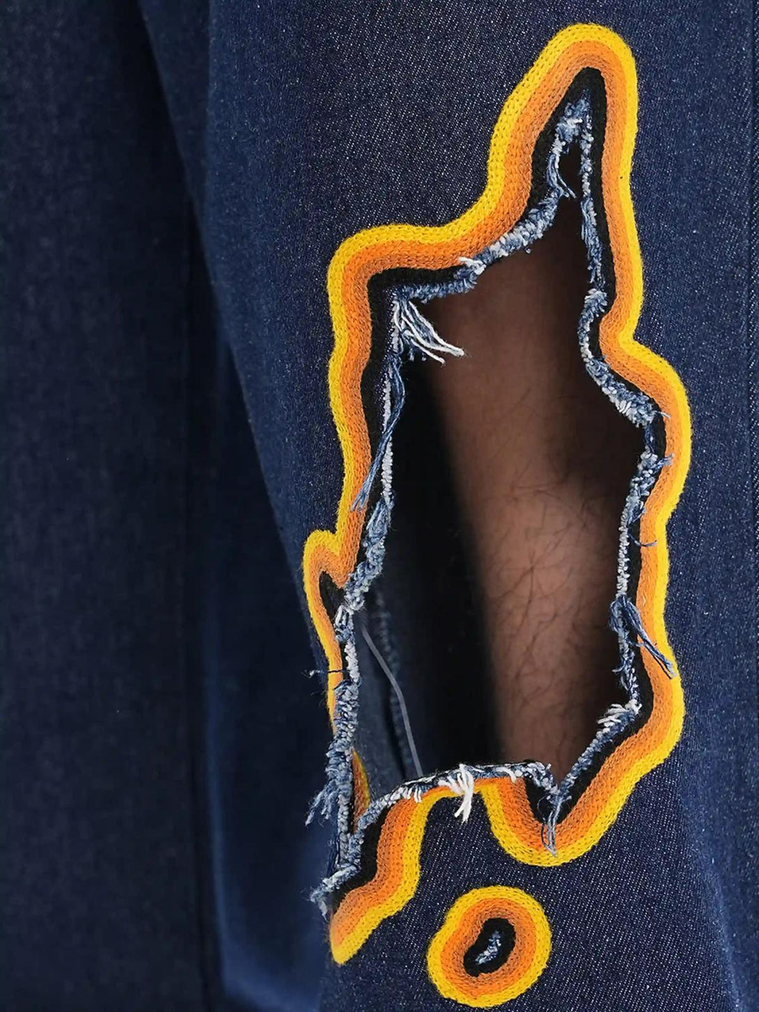 Intricate look at TALISHKO's flame-scarred embroidery on denim, featuring vivid orange accents.