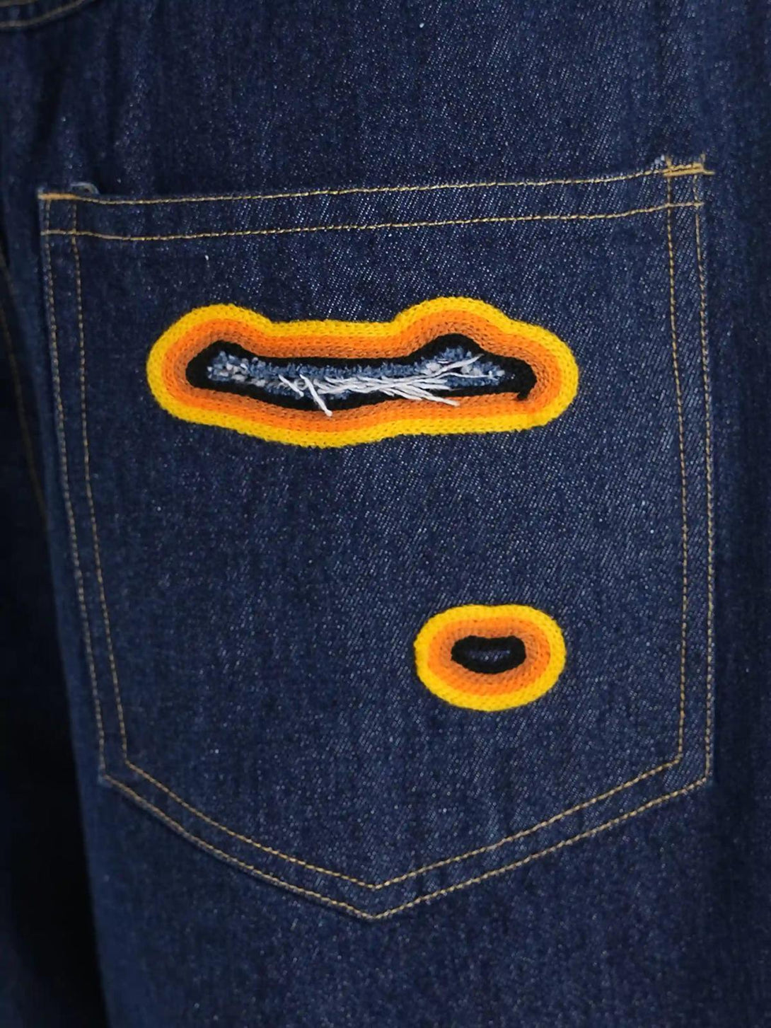 Focusing on TALISHKO's unique flame-scarred embroidery with vibrant orange accents on denim.